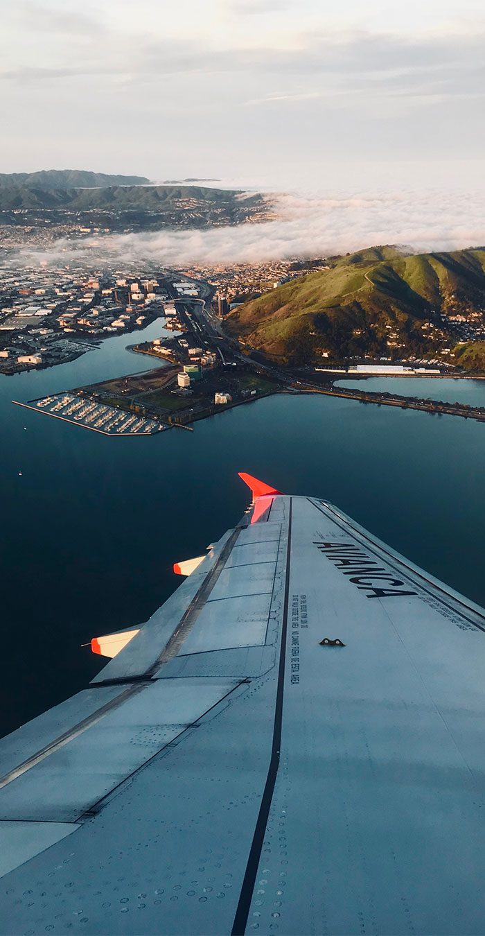 Airplane wing over coastal city and hills. Airplane wing over coastal city and hills.