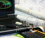 Laptop, blueprints, and calculator on desk.