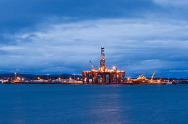 Offshore oil rig illuminated at dusk on calm waters.