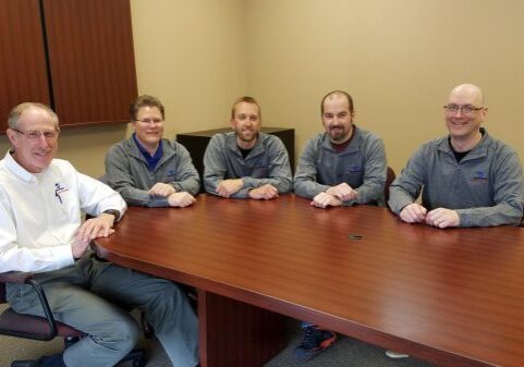 Four men sitting around a wooden conference table in a meeting room.