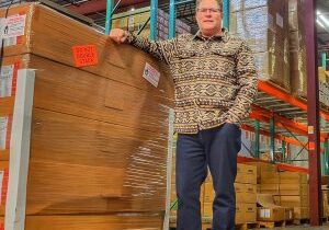 Man standing in a warehouse next to stacked wooden panels.